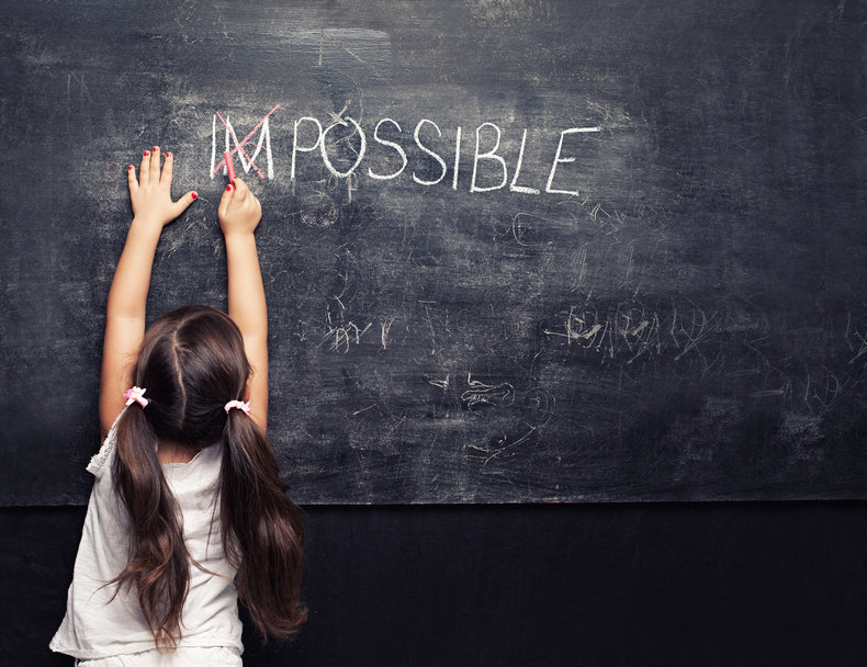 cute little girl putting a cross over impossible on blackboard